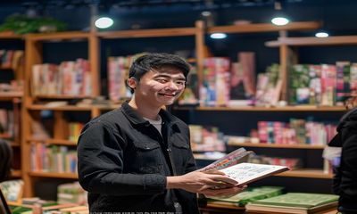 海角网读书圈直播现场，主播手持书籍向观众推荐2026年夏季必读书单，书架背景整洁温馨